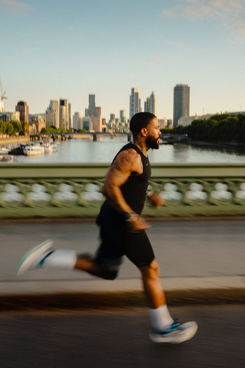 A runner wearing white crew socks during a sunset run across a bridge with a city skyline background.