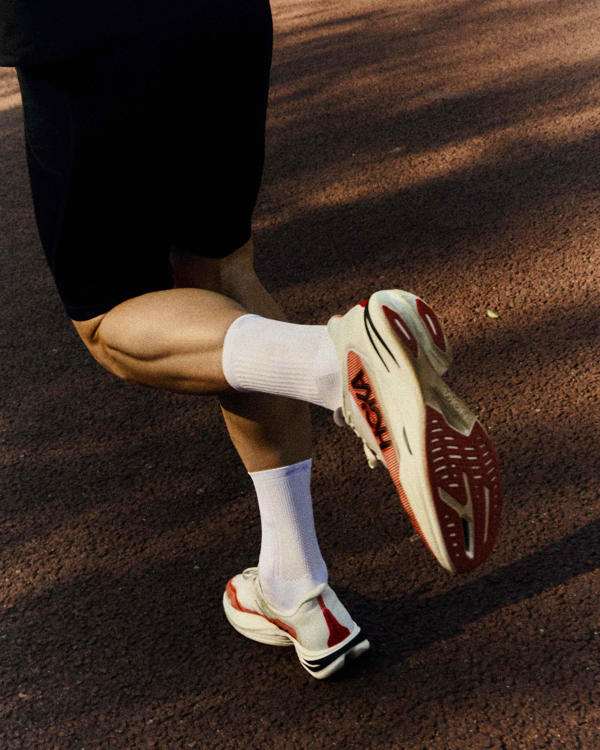 Close-up action shot of a runner's foot in motion, wearing a white POP Running Co performance sock paired with a technical running shoe.