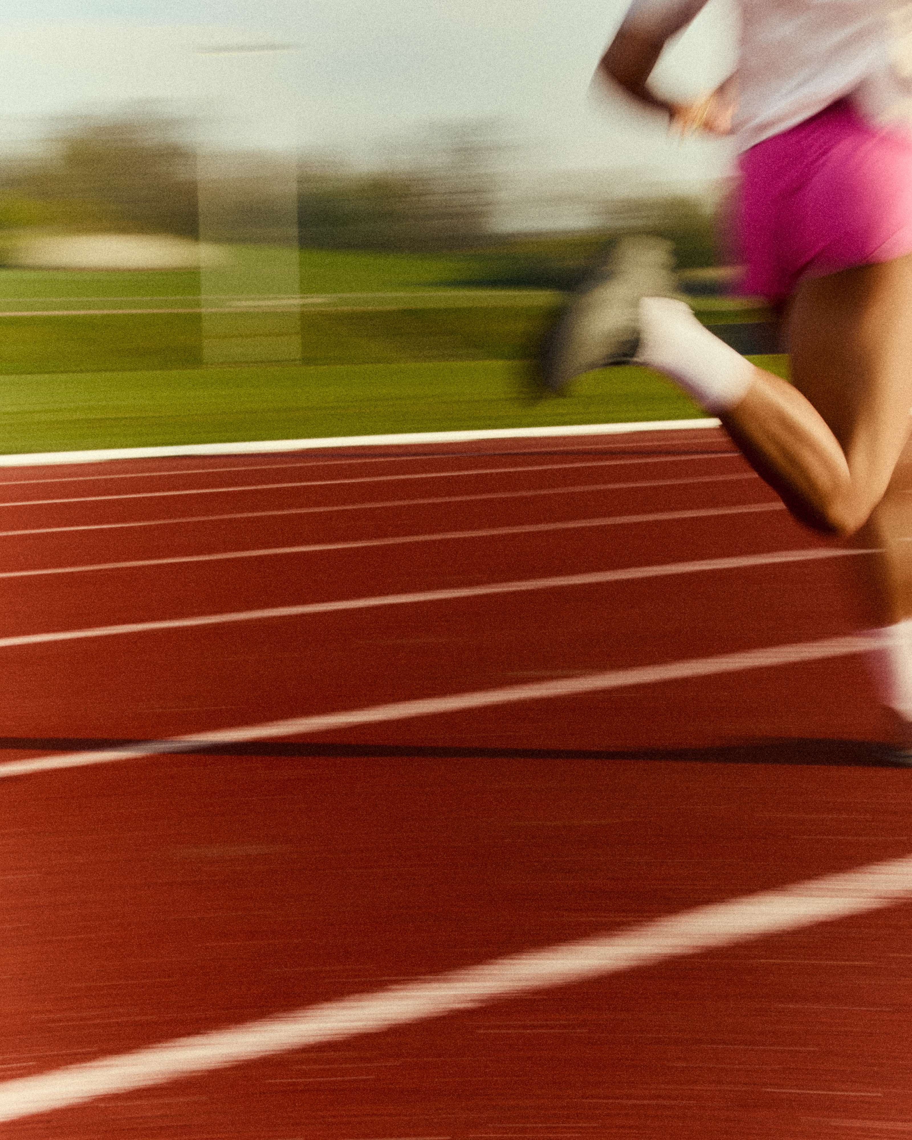 Action shot of a runner on a red track wearing white POP Running Co crew socks, highlighting speed and performance gear.