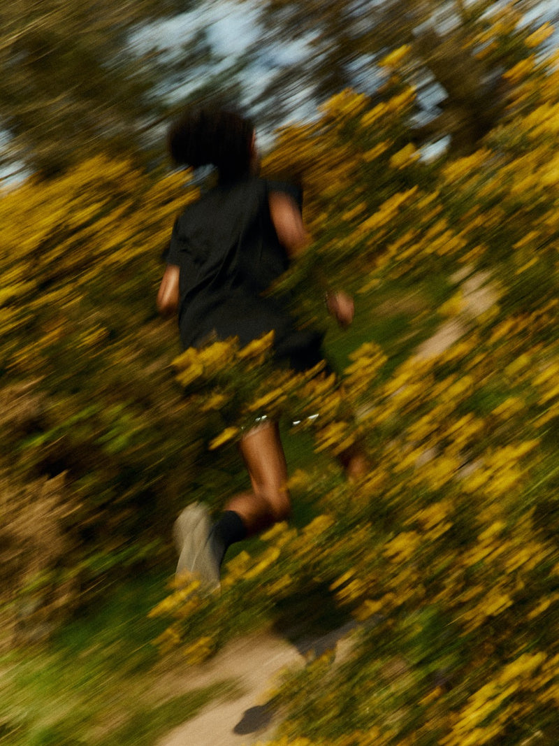 Dynamic motion blur shot of a runner wearing performance socks while navigating a scenic trail surrounded by yellow flowers.
